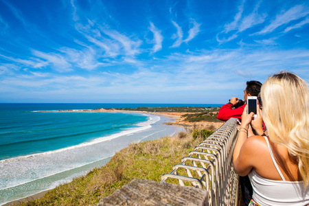Tourist girl take a photo with smartphone in mountains with seaside view to the ocean above some cliffs,The Great Ocean Road, Victoria, Australiaのeditorial素材