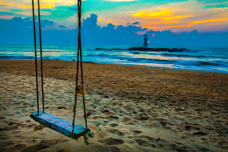 swing on the beach,sunset and beach. Beautiful sunset above the sea and lighthouse on the rockの写真素材