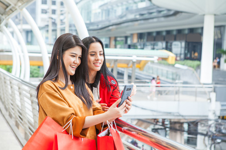 Portrait of young smiling modern beautiful women with shopping bags and mobile phone and shopping bags in city backgroundの写真素材