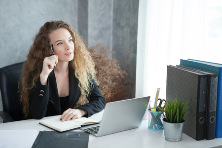 young business woman sitting in the office is thinking about idea in front of a laptop looking upの写真素材