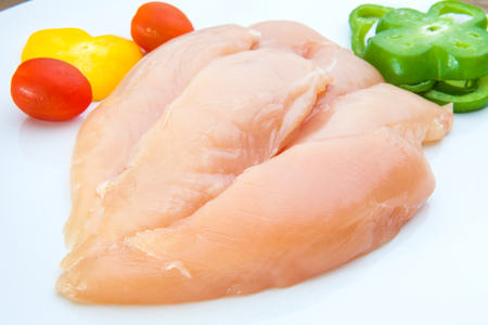 Raw chicken breasts and spices on white plateの写真素材