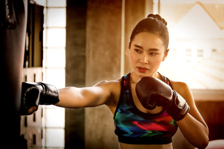 Beautiful athletic Asian Boxer woman punching bag with Boxing Gloves in fitness gym.sport girl in sportswear exercising or workoutの写真素材