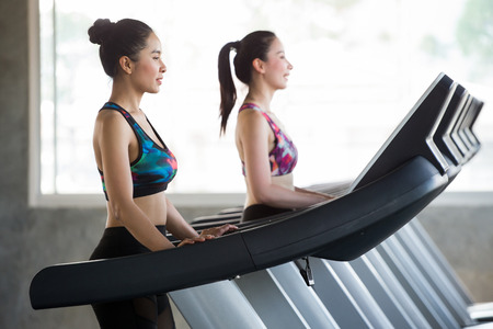 group of young asian people walking on treadmills warm up in sport gym  . two fitness woman runner on running machine in morning time . workout .training . exercise. healthy lifestyle .の写真素材