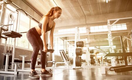 young fitness sport girl doing exercise squat with weight barbell plate in gym.woman in sportswear workout strengthen pumping up the musclesの写真素材