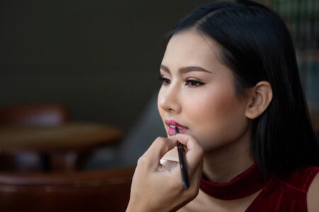 Makeup artist man applies lipstick painting lips of young beauty model on Backstage , asian womanの写真素材