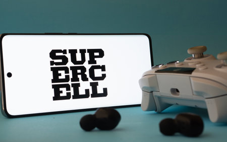 Dhaka, Bangladesh- 23 Mar 2025: A smartphone with a Supercell icon next to a controller and earbuds...