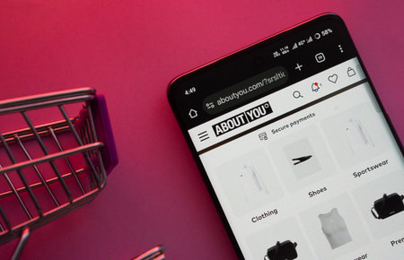Dhaka, Bangladesh- 21 Nov 2025: A smartphone displaying the About You website with a shopping cart is shown on a vibrant background.のeditorial素材