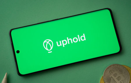 Dhaka, Bangladesh- 19 Sep 2025: Uphold logo on smartphone screen near Bitcoin coin and QR code on background.のeditorial素材