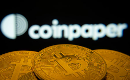 Dhaka, Bangladesh- 19 Sep 2025: Close-up of Bitcoin coins with the Coinpaper logo visible on a screen in the background.のeditorial素材