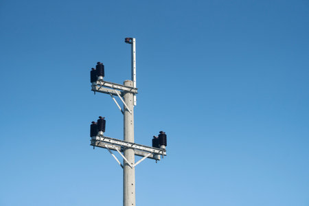 An electric pole with insulators and wires set against a clear blue sky on a bright dayの写真素材