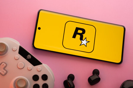 Dhaka, Bangladesh- 17 June 2025: Smartphone with rockstar games logo, game controller, and earbuds on a pink background.のeditorial素材