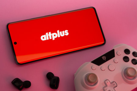 Dhaka, Bangladesh- 08 Apr 2025: A smartphone displaying the AltPlus Inc logo next to a gaming controller and earbuds on a pink surface.のeditorial素材