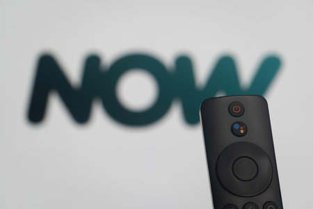 Dhaka, Bangladesh- 21 Jan 2026: Close-up of a smart TV remote control against a blurred NOW TV logo.