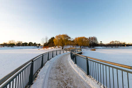 Empty bridge in a park in the winter, above a snow covered river.の写真素材