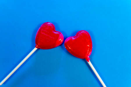 Shot of two heart-shaped lollipos next to each other on a blue background.