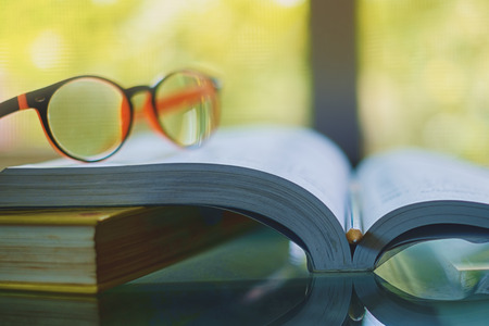 Glasses placed on the opened book with blurred natural background and vintage retro color tone