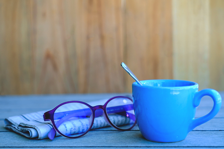 Blue coffee cup with newspaper and eye glasses on the wooden tableの写真素材