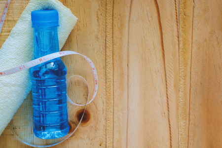 Drinking water bottle, towel and measure tape on wooden table with copyspace, Exercise and healthy concepts.の写真素材