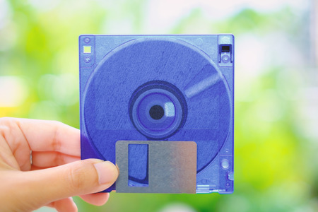 Hand holding a floppy disk against blurred background, old technology and legacy industrial computer equipmentの写真素材