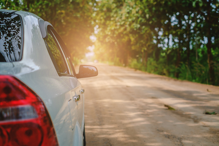 White car on rural road amidst green trees with sun lightの写真素材