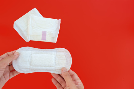 Hand holding feminine sanitary napkin, an absorbent item worn by a woman while menstruating, on red...
