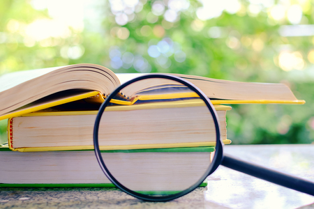 Books zoomed by the magnifying glass on blurred natural green background for learning and education conceptの写真素材