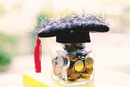 Square academic cap with the glass jar of coin on the book against blurred natural green background for education, finance and saving money conceptの写真素材