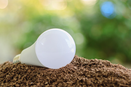 LED light bulb on soil against blurred natural green background with copy space for saving energy...