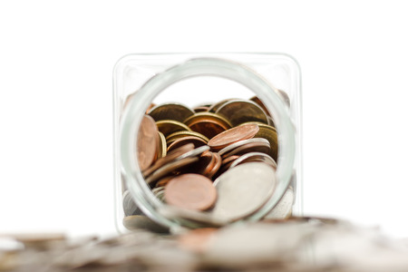 Selective focus of coin in the glass jar with blurred money in foreground against white background...