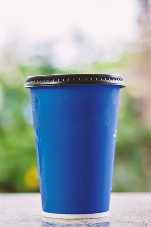 Blue paper cup of iced coffee on blurred natural background for drinking and beverages conceptの写真素材