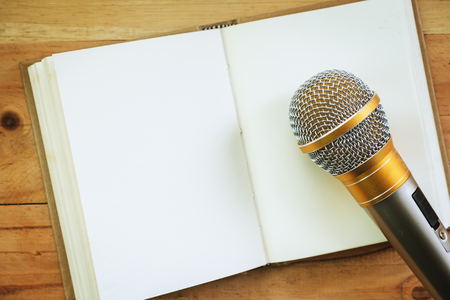 Microphone on an opened notebook on wooden background for speaking, learning and teaching conceptの写真素材