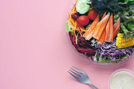 Fresh vegetables with salad dressing and fork on pink background and copy space for diet and heathy eating conceptの写真素材