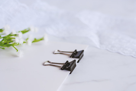Binder clip binding white paper card with decorative flower and lace ribbon on white marble background for office and school supplies concept, selective focus and DOFの写真素材