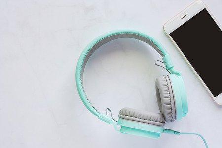 Smartphone with headphones on white marble background and copy space