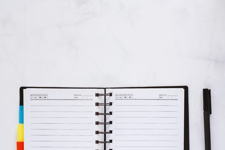 Opened spiral notebook with black pen on white marble background for workspace conceptの写真素材