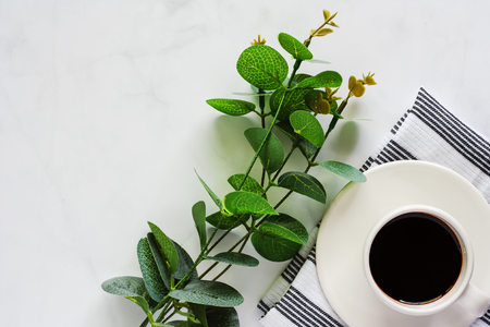 Cup of coffee with saucer, napery, leaf bouquet on white marble background for drinks and beverage conceptの写真素材