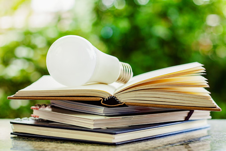 LED lamp on stack of opened books against blurred natural green background for education conceptの写真素材