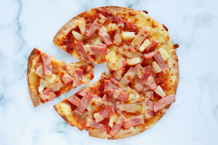 Delicious pizza with pineapple, ham slice, bacon slice, mozzarella cheese, pizza sauce on white marble background for fast food and ready to eat conceptの写真素材