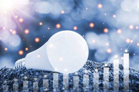 LED light bulb on soil against blurred natural background with growing graph and light effect for...