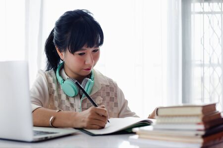 Asian woman writing on the paper, using laptop and working at home for businessの写真素材