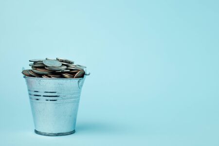 Full of money coins in a tin bucket on blue background for investment, business, finance and saving money conceptの写真素材