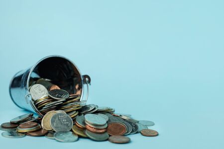 Pile of money coins with a tin bucket on blue background for investment, business, finance and...