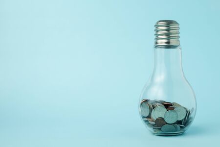 Coins in light bulb bottle shape on blue background with copy space for investment, business,...