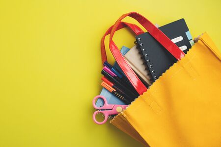 Learning supplies with notebook, coloured pen and scissors in yellow bag on yellow background with copy space for education and back to school conceptの写真素材