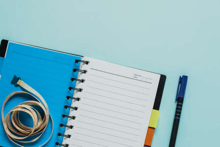 Notebooks with measure tape on blue background for healthy diet taking notes conceptの写真素材