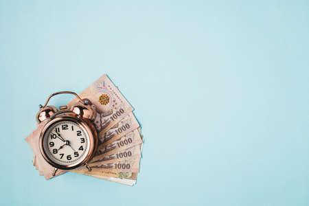 Bell alarm clock  with Thai currency, 1000 Baht, money banknote of Thailand on blue background for business, finance and time management conceptの写真素材
