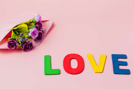 LOVE word with artificial purple rose bouquet in envelope on pink background for love and Valentine's day conceptの写真素材