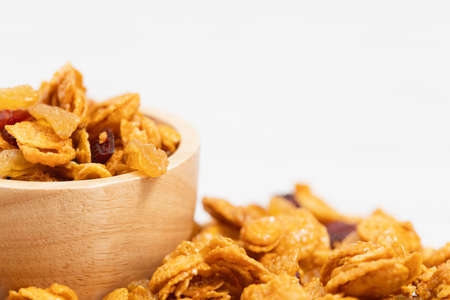 The wooden bowl of caramel cornflakes with raisins on white background for healthy eating and...