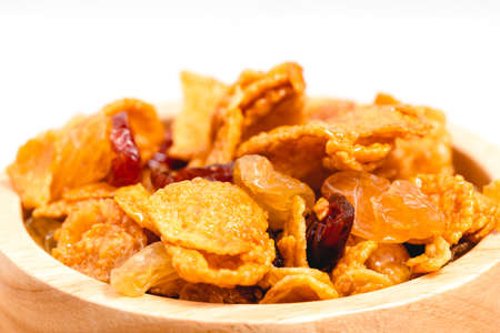 The wooden bowl of caramel cornflakes with raisins on white background for healthy eating and breakfast conceptの写真素材
