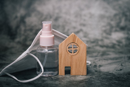 Wooden house model with the bottle of alcohol gel and hygiene face mask on dark background for healthcare, self-quarantine and staying home in virus  situation conceptの写真素材